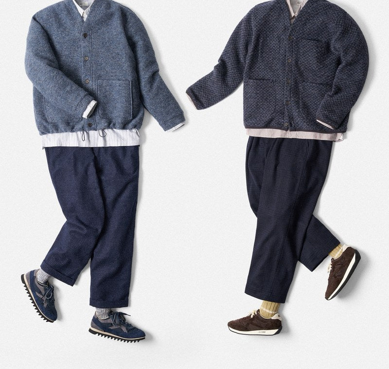Dois conjuntos Universal Works dispostos na horizontal: casacos de malha de lã azul-escuro e azul-claro, camisa branca, calças azuis e sapatilhas.